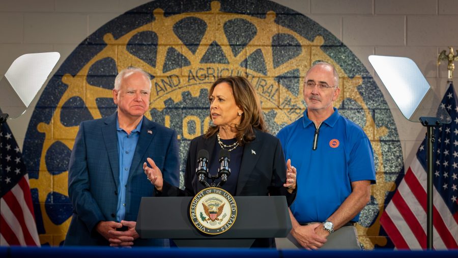 Vice President Kamala Harris addresses United Auto Workers members at UAW Local 900 in Wayne, Michigan, alongside her running mate, Minnesota Gov. Tim Walz (left) and UAW President Shawn Fain (right), on Thursday, Aug. 8, 2024.