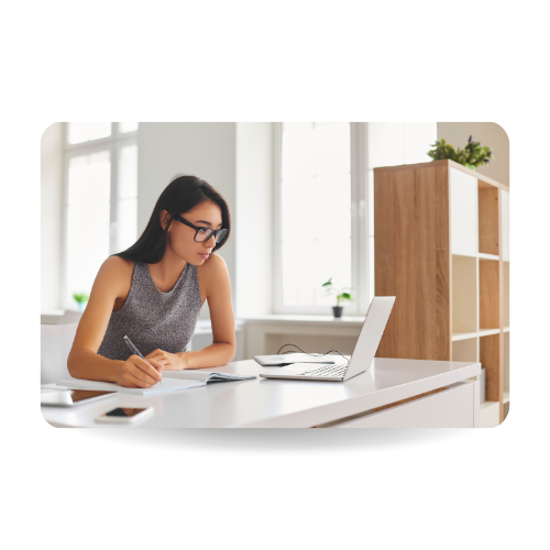 There is a woman in a desk in front of a laptop and writing in a notebook. 