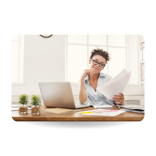 There is a girl sitting in a desk in front of a laptop and carrying some documents