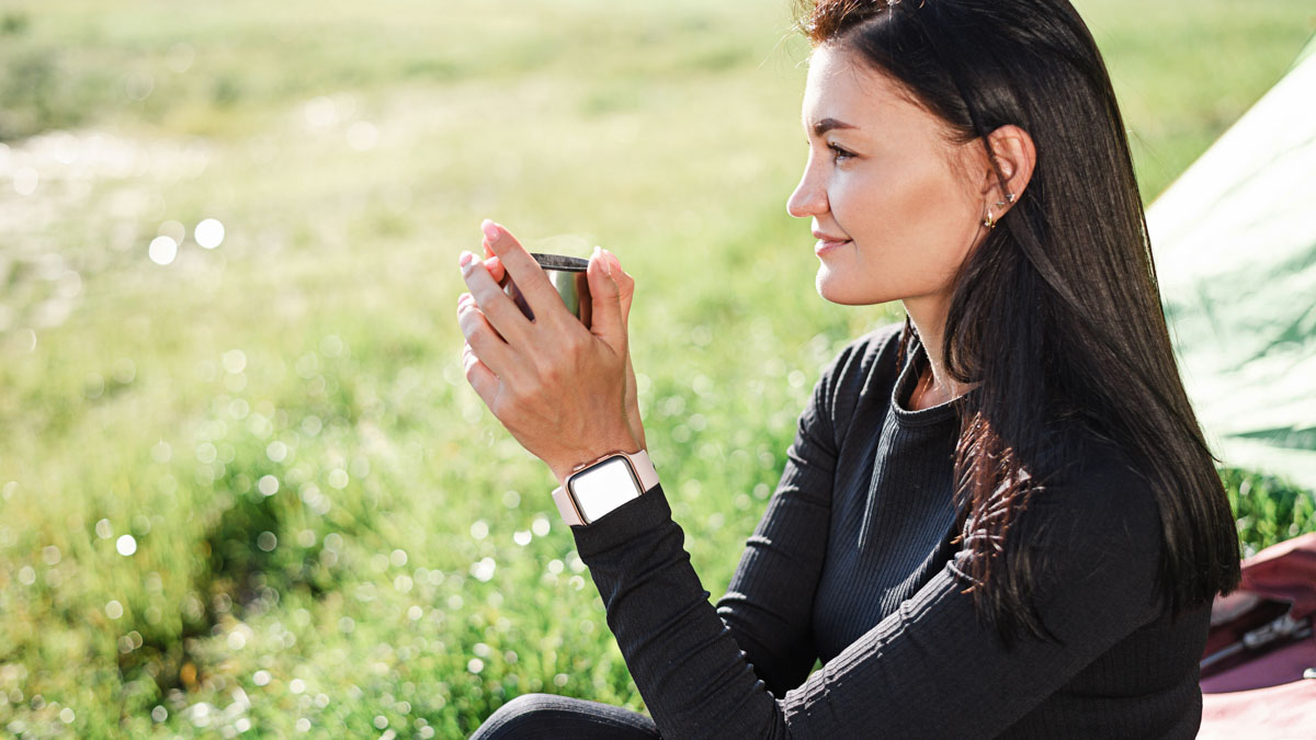 Female Athlete Sitting In Grass On Recovery Day Drinking Adaptogen Tea For Recovery Benefits