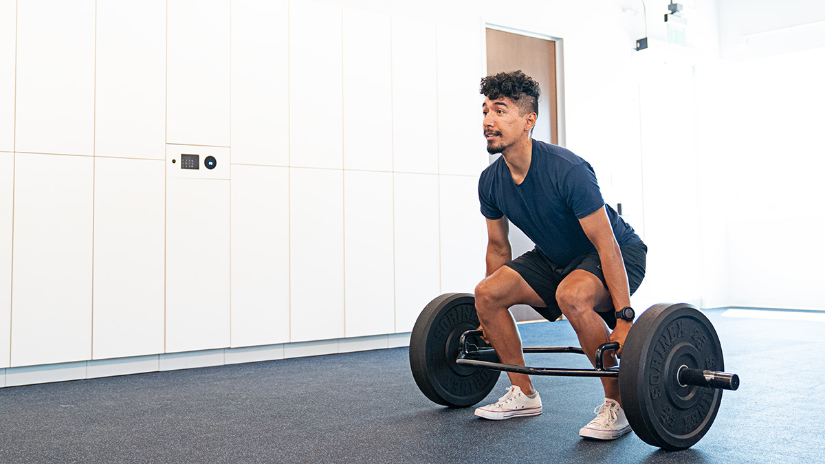 Male Runner Athlete In The Gym Doing Strength Training With A Hex Bar Deadlift