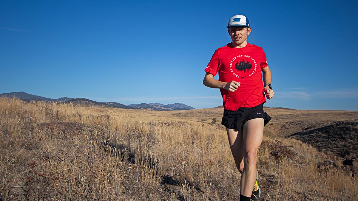 Male Runner In Tshirt, Hat And Shorts Doing A Training Run On A Sunny Day With Blue Sky In The Background