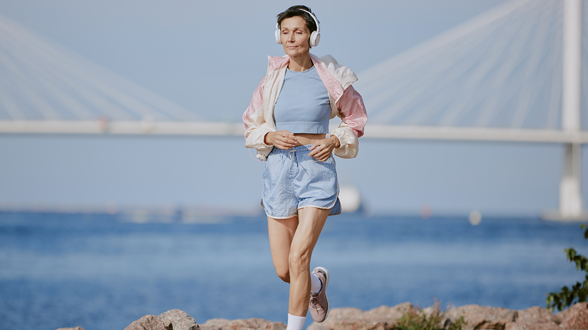 Postmenopause Woman Training Running In Shorts And Tshirt Outside With Ocean In Background