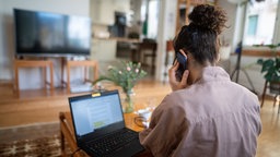 Eine Frau nimmt am Wohnzimmertisch an einer Telefonkonferenz teil