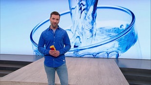 Daniel Aßmann steht im Servicezeit-Studio. Im Hintergrund sieht man das Bild von einem Glas voller Wasser.