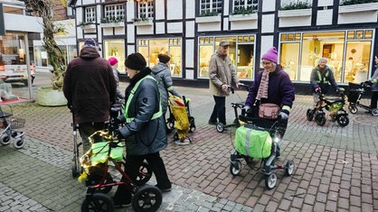 Die Innenstadt einer Kleinstadt. Mehrere Senioren mit Rollatoren gehen im Kreis