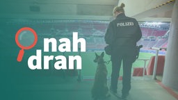 Eine Polizistin steht mit einem Diensthund in einem leeren Fußballstadion und schaut auf die Tribünen 