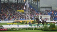 Eine Dressurreiterin reitet in einem gut gefüllten Stadion.