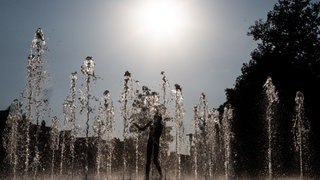 Kinder vergnügen sich in den Wasserfontänen eines öffentlichen Springbrunnens unter der Sonne