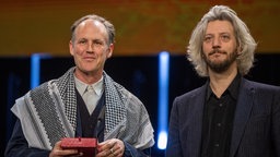 Der Filmemacher Ben Russell (l) mit einem Palästinensertuch auf die Bühne. Er äußerte Genozid-Vorwürfe wegen des israelischen Vorgehens im Gazastreifen. Aus dem Publikum kam Applaus.