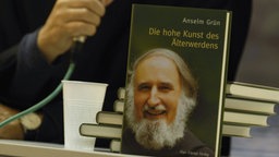 Anselm Grün im Hintergrund unscharf davor sein Buch "Die hohe Kunst des Aelterwerdens"