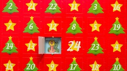 Ein roter Adventskalender mit Stern und Tannenmotiven. Das erste Türchen ist geöffnet. 