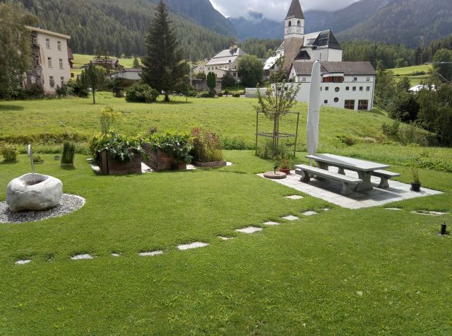 Gartenanlage aus Steintisch, Steinbrunnen, Hochbeet und grüner Wiese in Tarasp im Engadin.