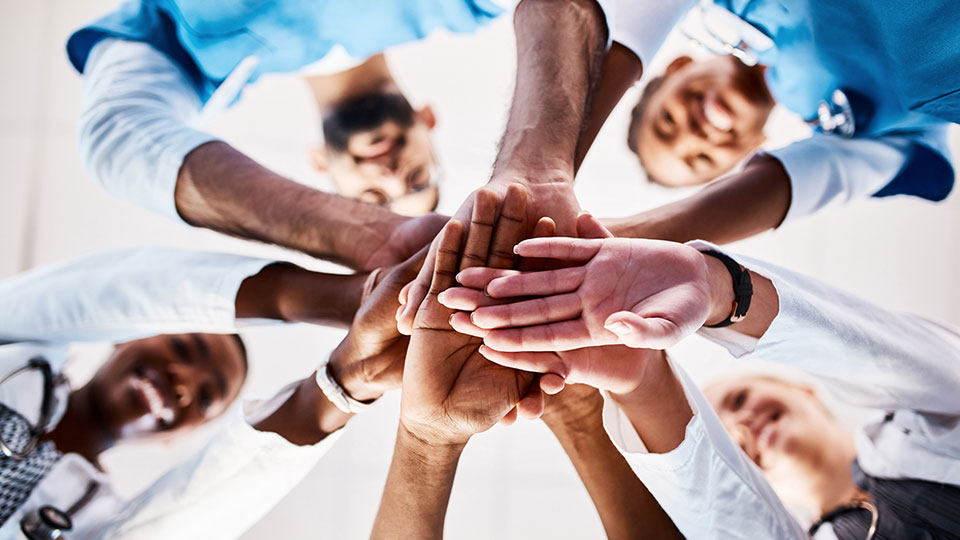 Pediatricians looking down in a circle with their hands together.