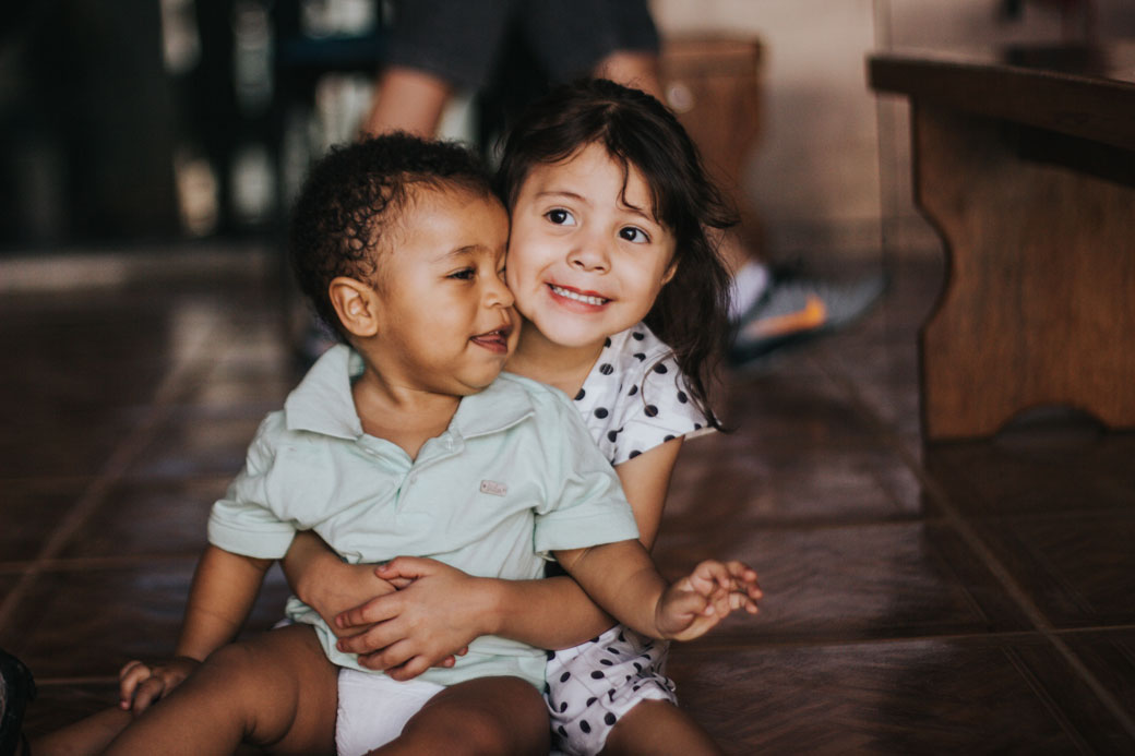 Sibling embracing other sibling sitting on the ground.