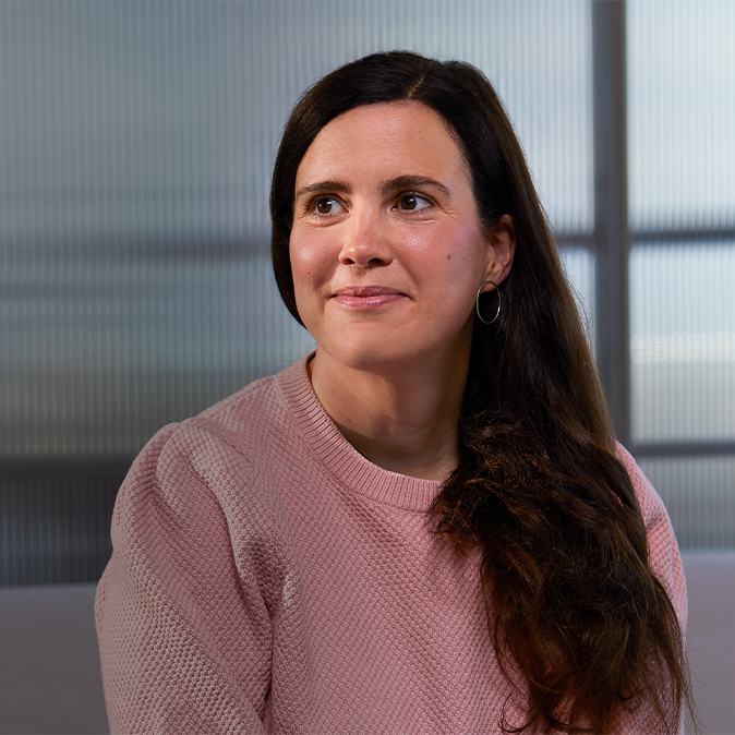 Lucie sitting indoors with a translucent glass wall behind her, smiling and looking to her right.