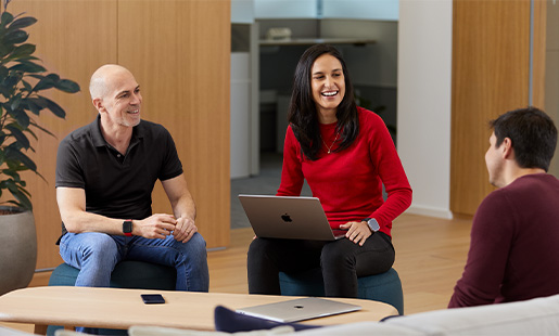 Camila laughing, sitting between two other Apple colleagues, with a MacBook on her lap.