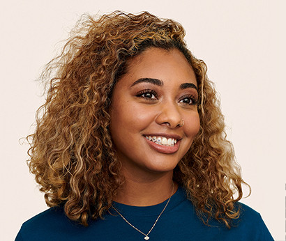 Apple Retail employee with shoulder-length hair and a necklace, smiling at the camera.