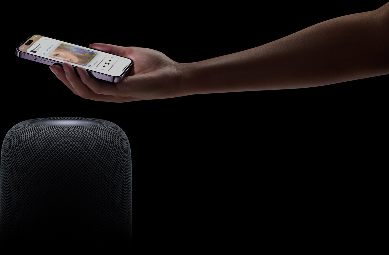 Eine Hand, die von rechts kommt, hält ein iPhone über einen HomePod Lautsprecher