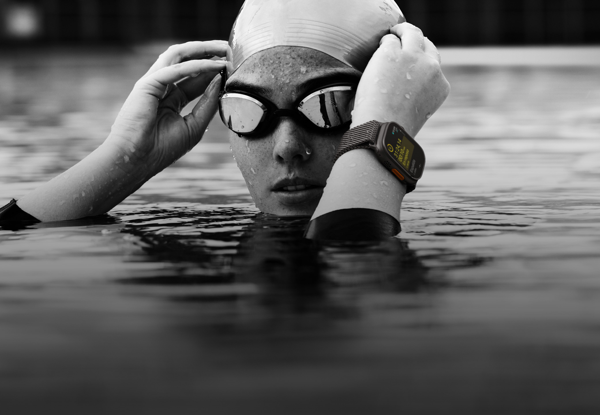 Una persona que lleva un Apple Watch Ultra 2 en una piscina y tiene la cabeza y las manos fuera del agua para ajustarse las gafas de natación.