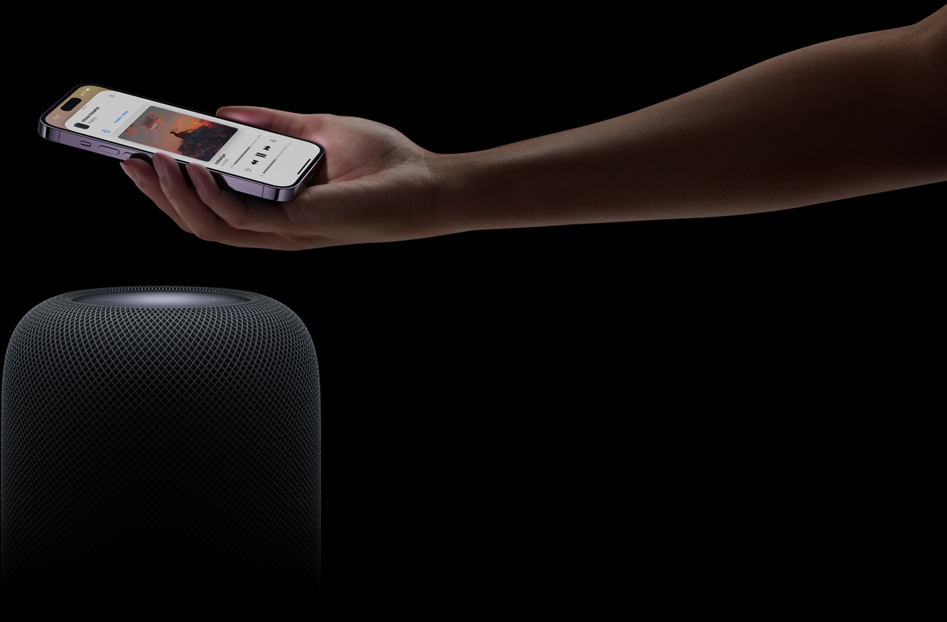 A hand coming in from the right side of the page holds an iPhone above a HomePod speaker