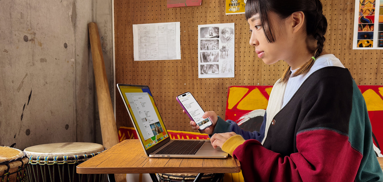 大学のサークルの部室で学生がMacBook AirとiPhoneを使ってメモを書いている。