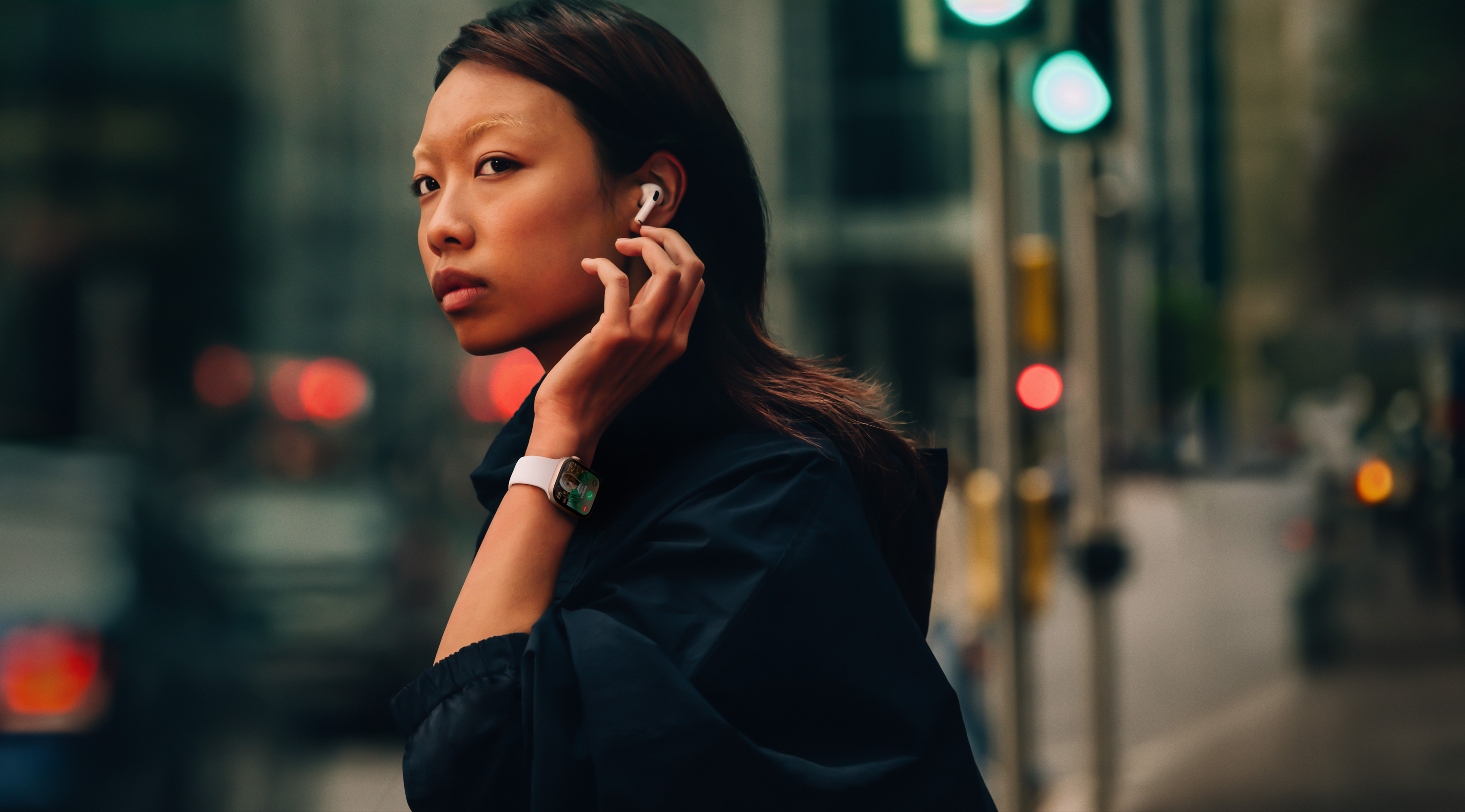 A woman on a street wearing Apple Watch Series 10 and AirPods.