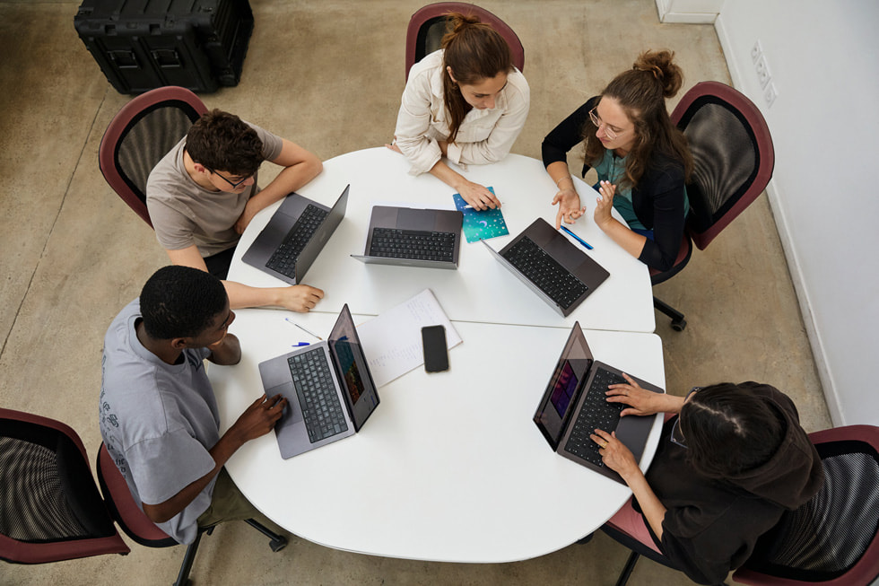 Photo aérienne de cinq élèves de l'Apple Foundation Program travaillant sur des MacBook autour d’une table.