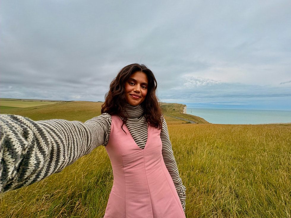 Una selfie con un paisaje cubierto de pasto que lleva hacia el mar de fondo. 