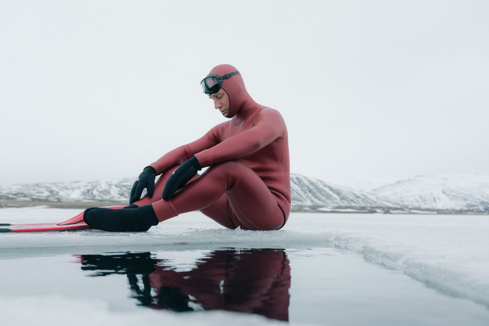 Ant Williams sits beside an opening carved in ice, preparing to dive.