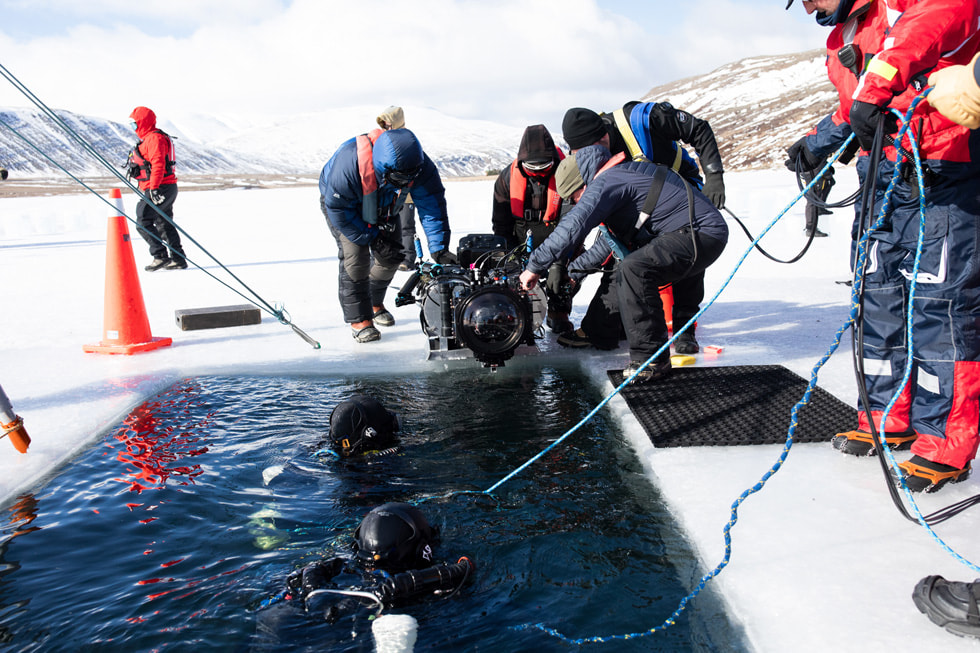 A behind-the-scenes shot of a camera and crew on a frozen body of water shows the making of the “Ice Dive” episode of “Adventure.”