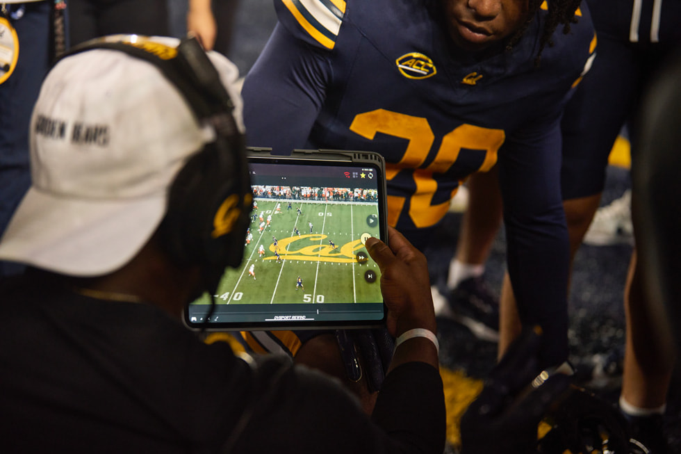 Cal coaches and players huddle around iPad during a football game.