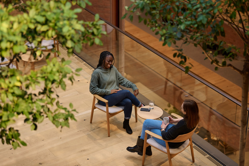 Two people sit at a small table indoors and drink coffee.