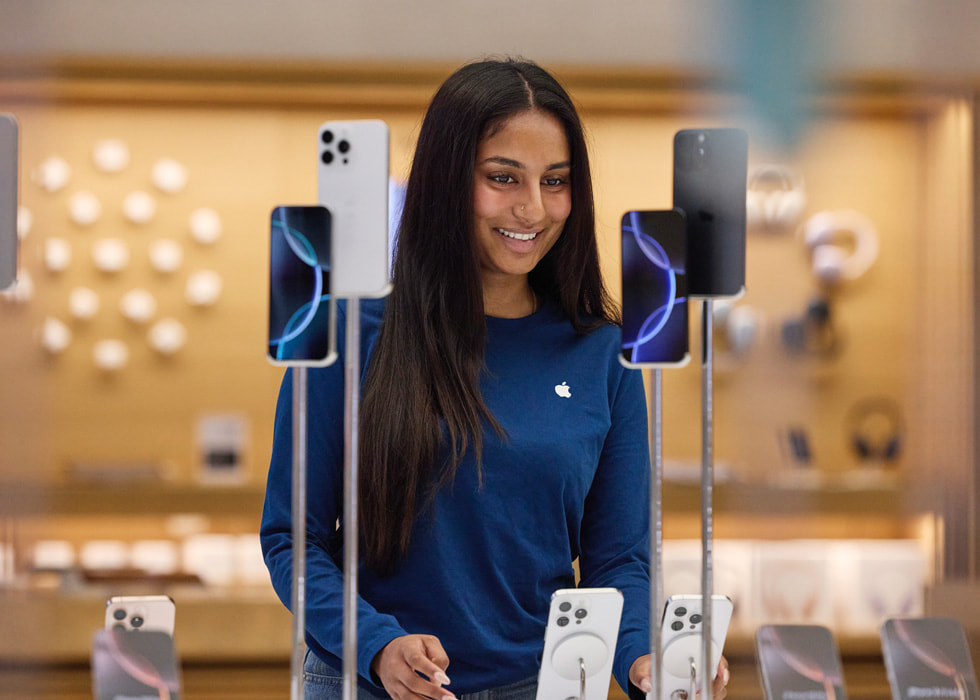 Inside Apple Regent Street in London, a team member looks at an iPhone in front of the iPhone 16 display.