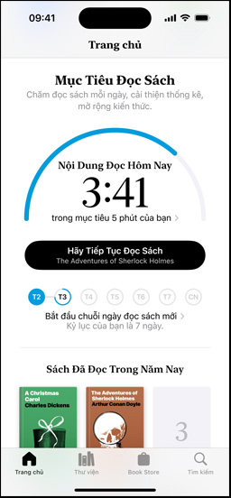 Màn hình iPhone hiển thị giao diện Mục Tiêu Đọc trong ứng dụng Sách. Một vòng tiến trình ở phía trên. Bên dưới vòng tiến trình là công cụ theo dõi chuỗi thành tích đọc sách hàng tuần. Ở dưới cùng là mục Sách Đã Đọc Năm Nay, bao gồm một hàng hai quyển sách, kèm một ô trống cho quyển thứ ba