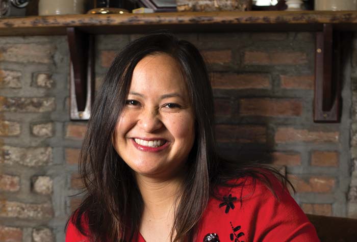 Photo of Marissa Aroy seated in front of a hearth