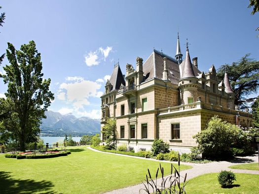 Schloss Hüngee in Hilterfingen mit grüner Wiese und Thunersee im Hintergrund