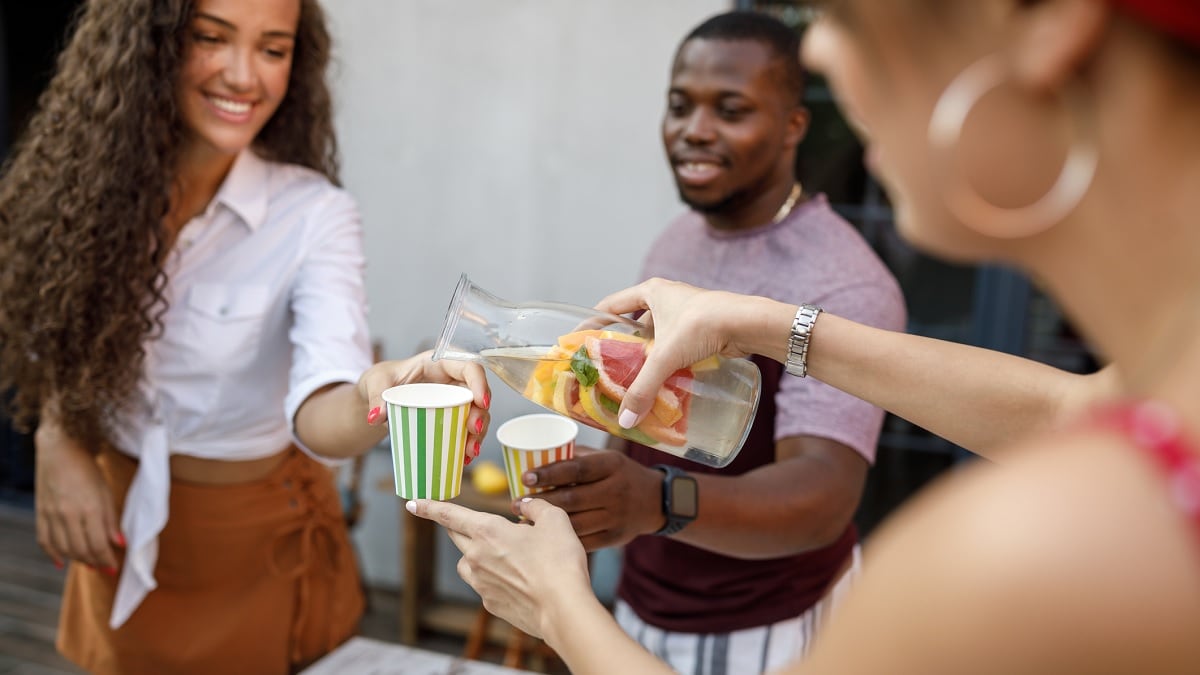 Mujer joven sirviendo agua con fruta para amigos en la fiesta