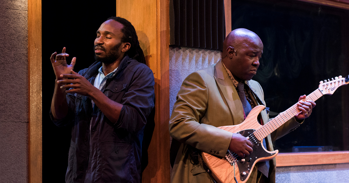 2 performers performing on stage. One is playing a guitar.