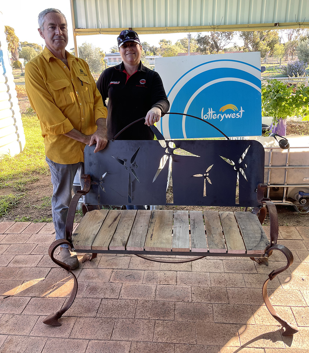 Two sculptors standing behind a sculptured sitting bench.