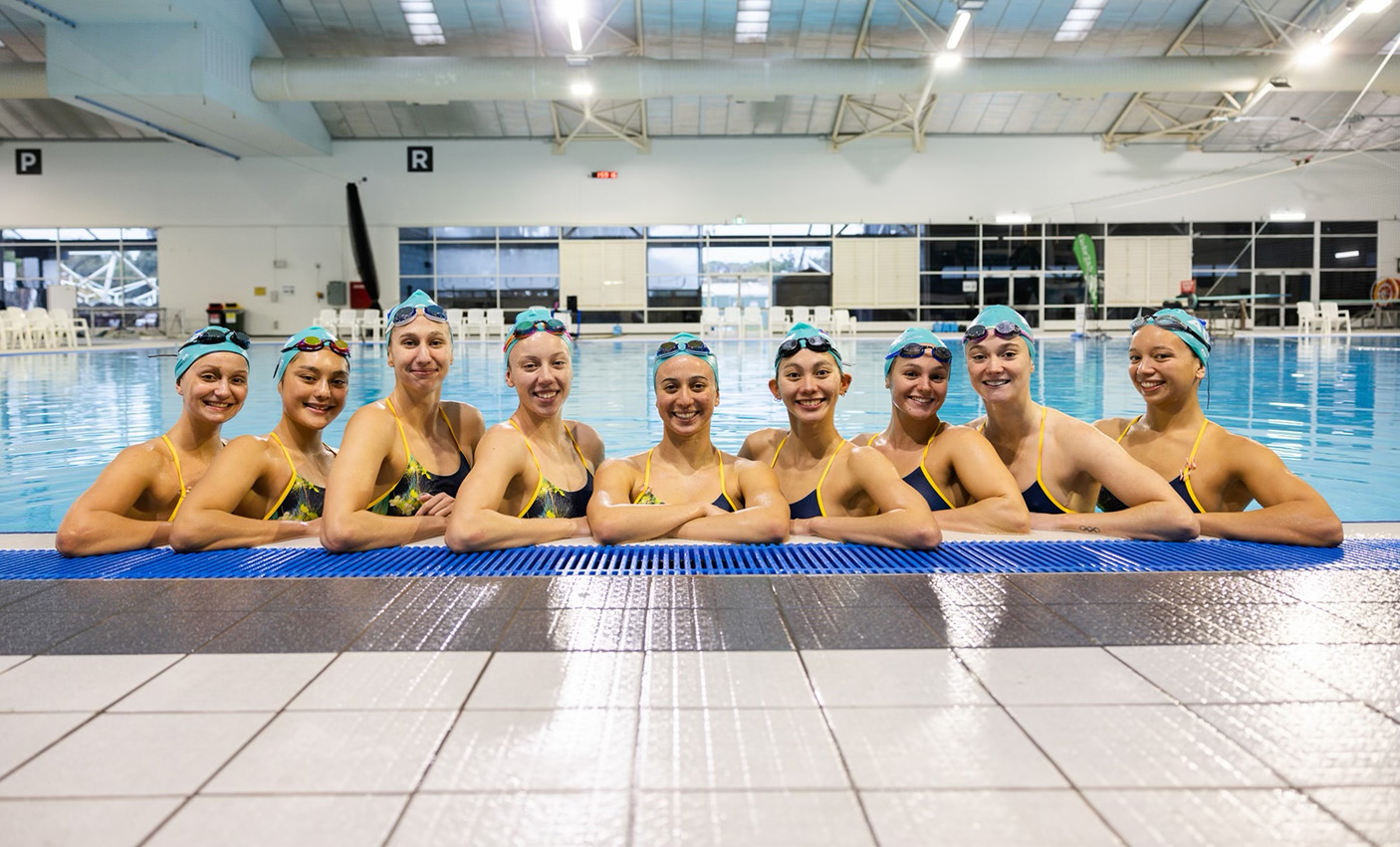 Artistic swimmers standing together at the edge of the pool.