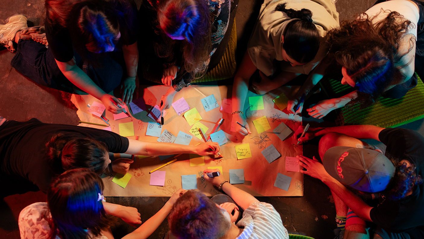 A group of young people around a table writing on sticky notes seen from above.