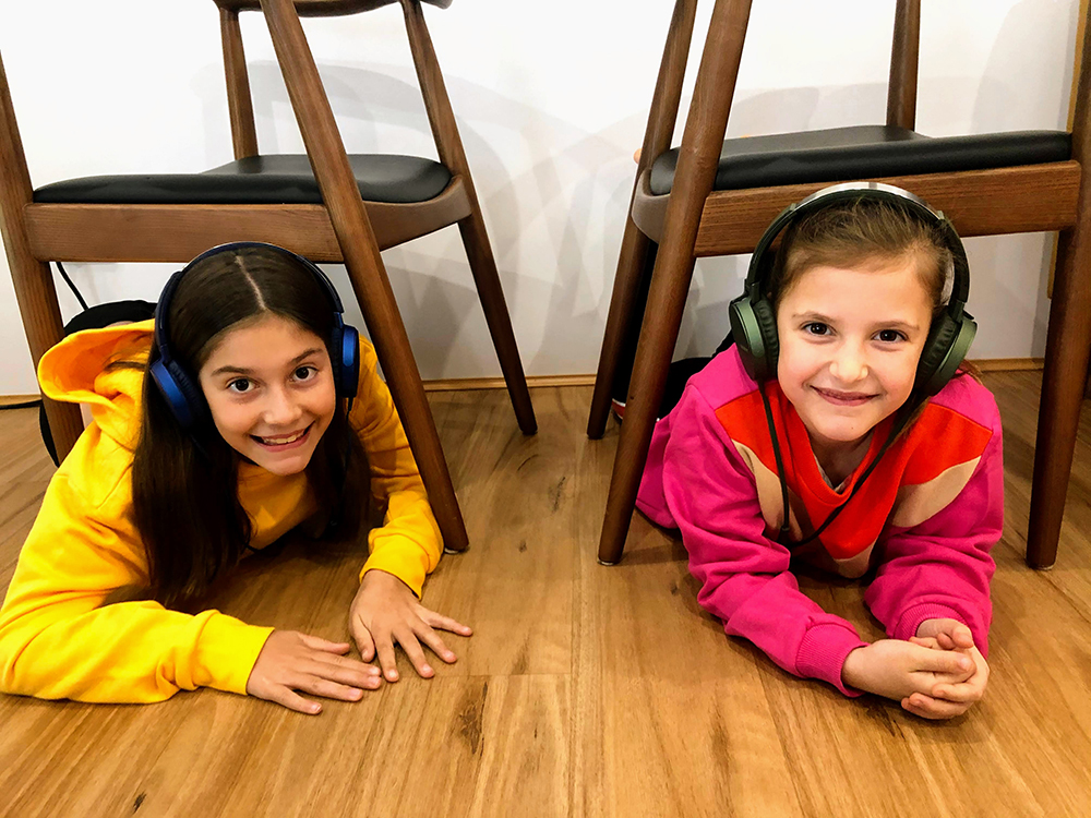 Two girls laying on a wooden floor.