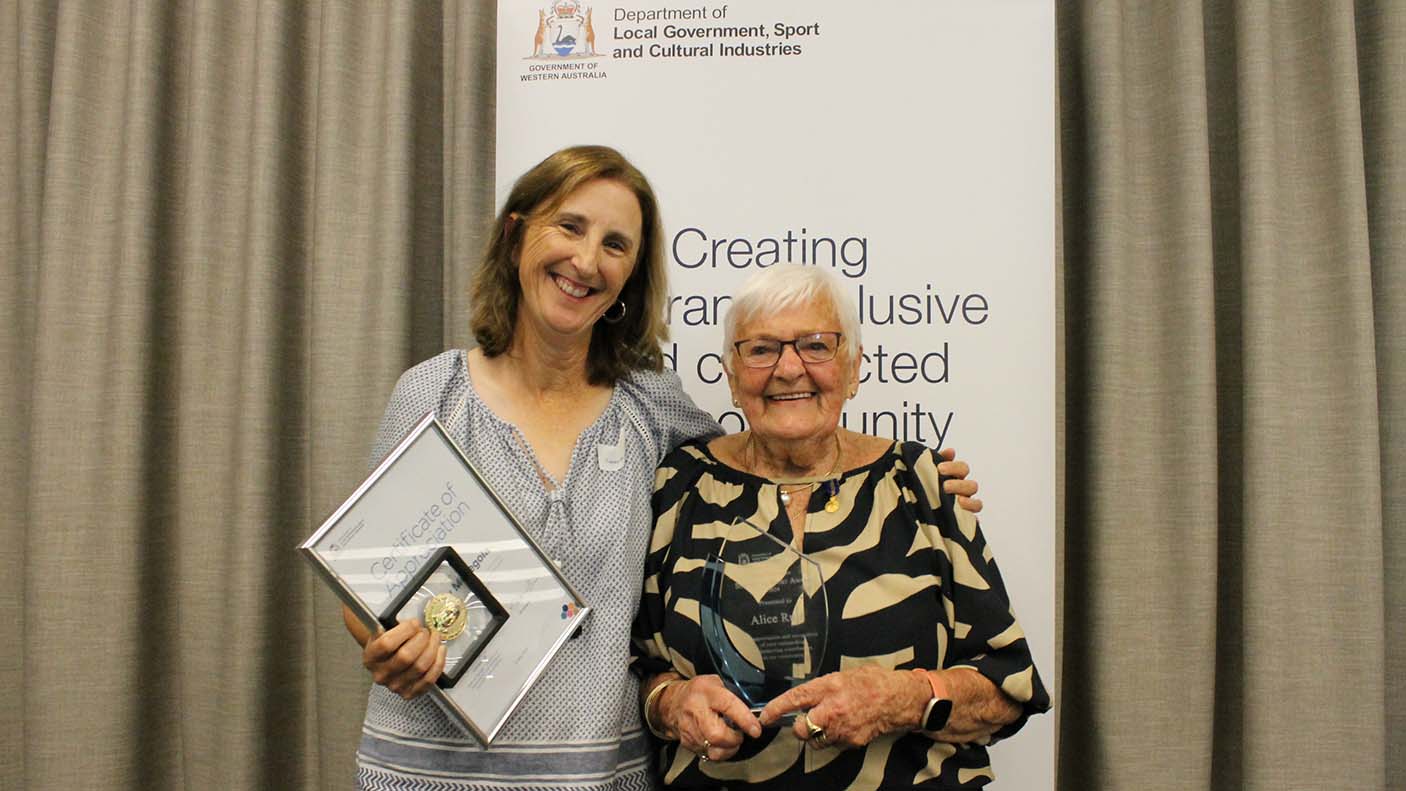 Photo of award winners holding framed certificate in front of a banner and curtain