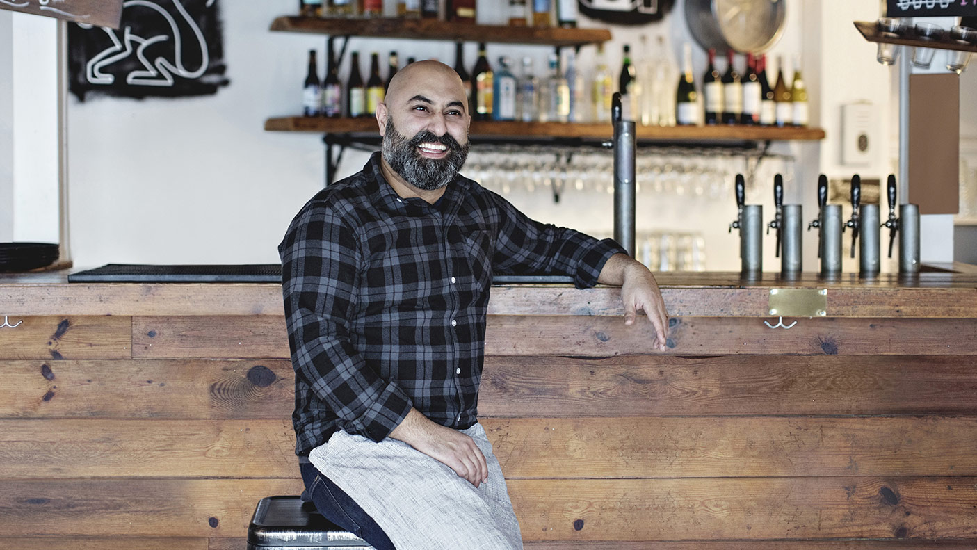 Confident smiling bartender sitting by bar counter