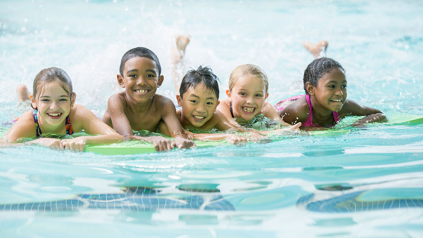 5 children line up on kickboards in a public swimming pool