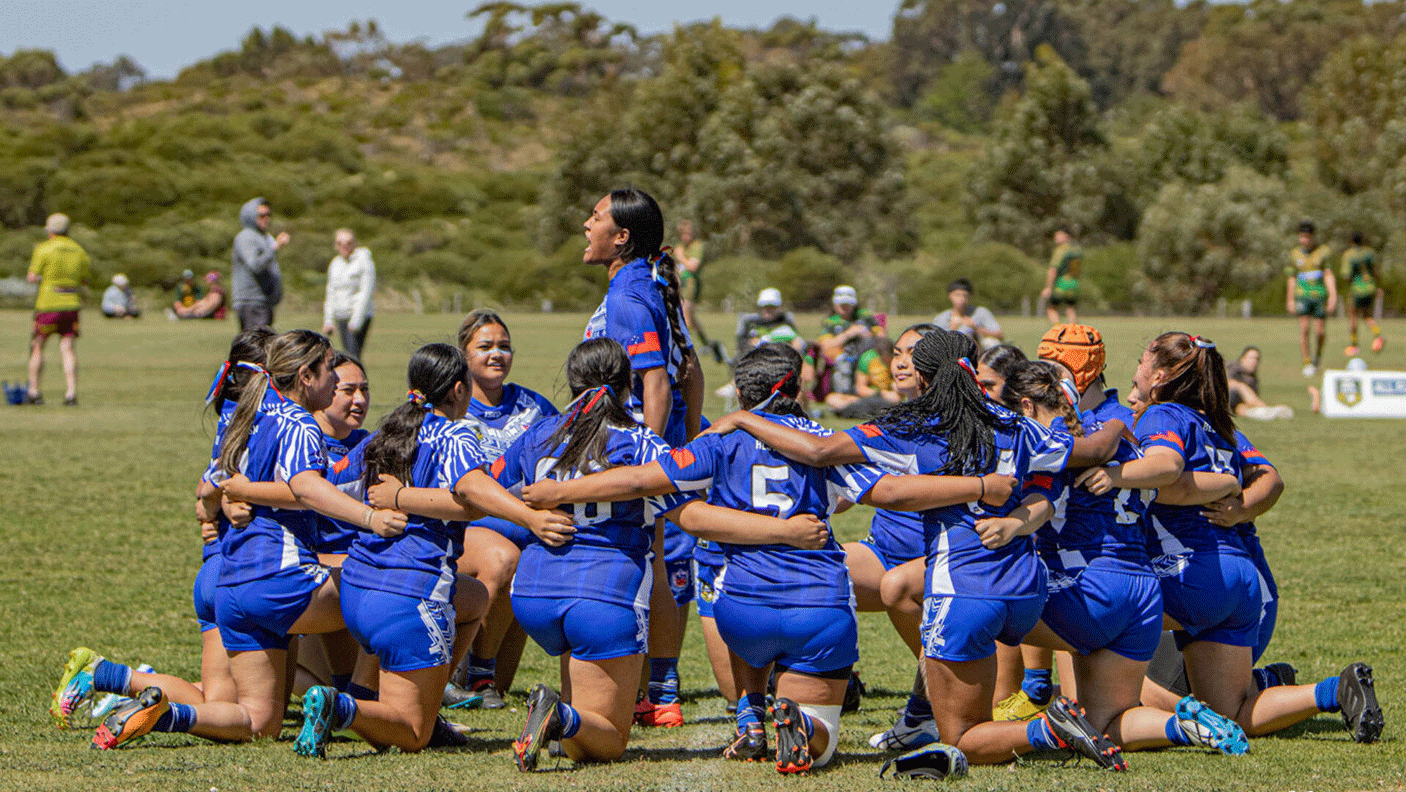 A group of female rugby players huddle on the sporting field