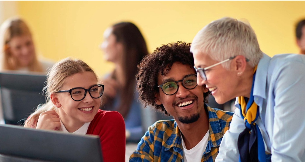 three people smiling around computer