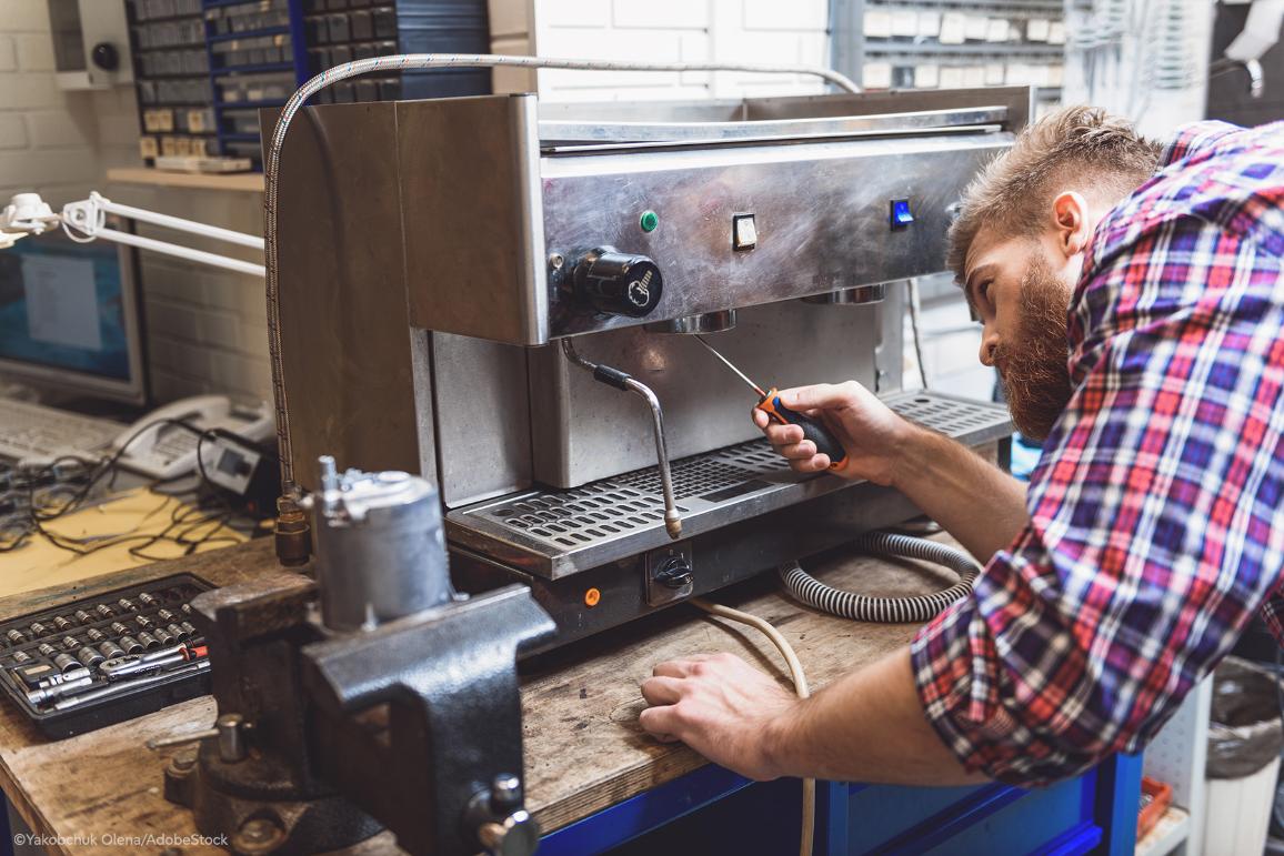 A repairman with a screwdriver fixing coffee machine on a working indoors table