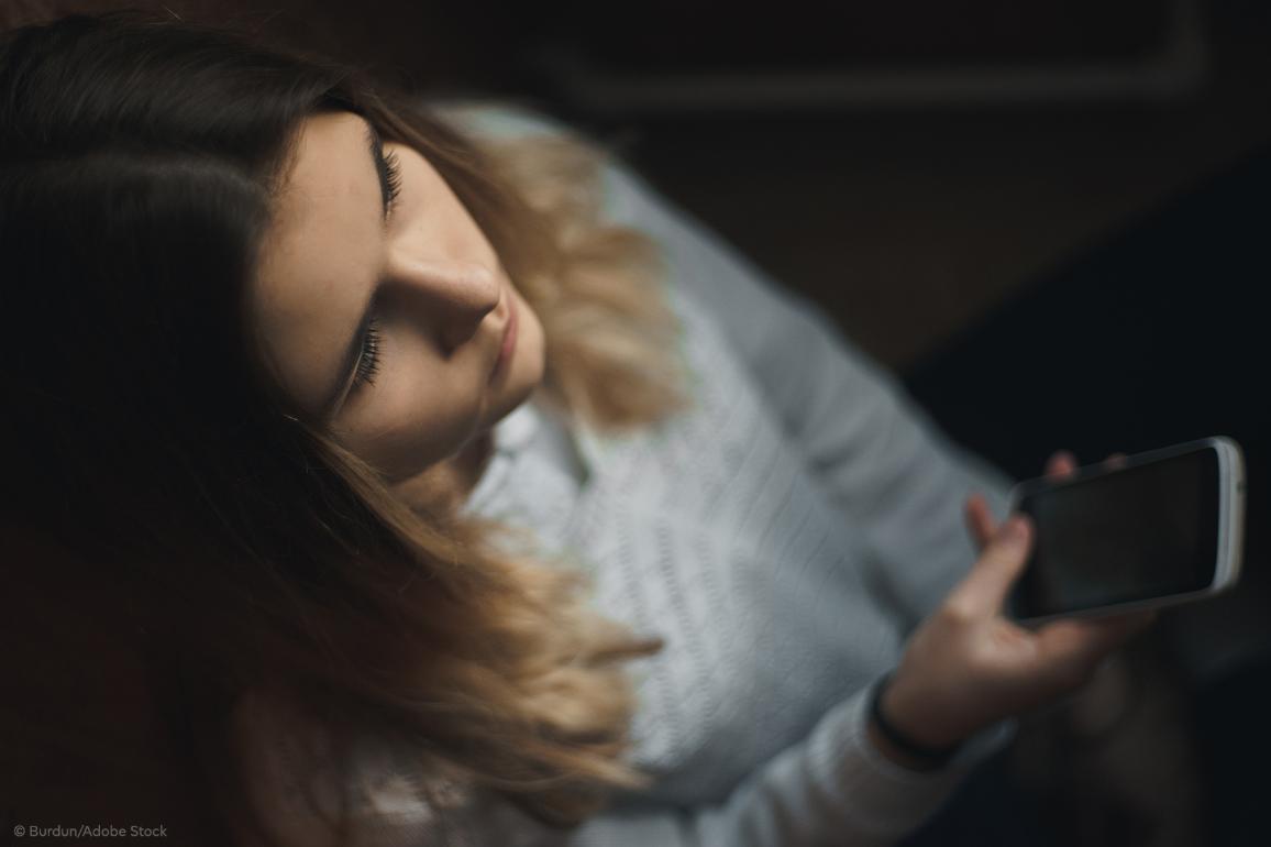 A teen girl victim of online harassment looking straight with a sad expression and her mobile phone in the hand.